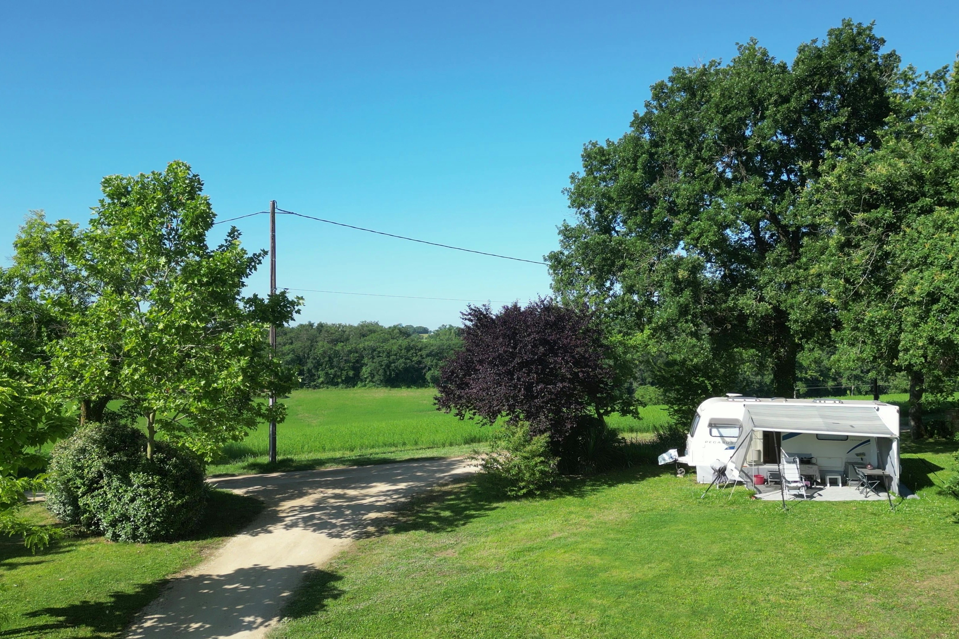 Wohnwagen auf einem grünen Campingplatz mit Rasen, Hecken und einem Kiesweg zwischen Bäumen.