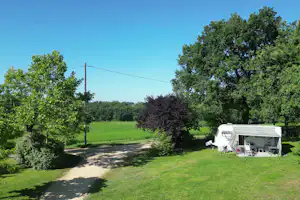 Wohnwagen auf einem grünen Campingplatz mit Rasen, Hecken und einem Kiesweg zwischen Bäumen.