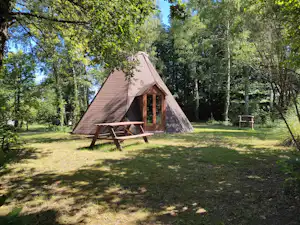 Campingzelt mit Holzveranda im Grünen, umgeben von Bäumen und Rasenfläche auf einem Campingplatz.