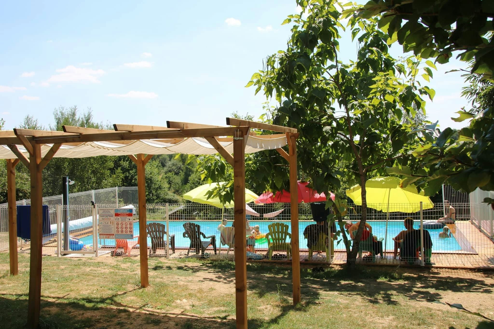 Poolbereich am Campingplatz mit Pergola, Liegestühlen und Sonnenschirmen, umgeben von Rasen und Bäumen.