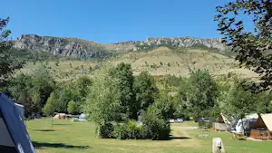 Campingwiese mit Zelten, Bäumen und Blick auf eine Berglandschaft im Hintergrund.