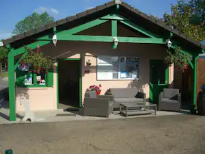 Grünes Wohnzelt mit Sitzgruppe aus grauen Polsterstühlen und Tisch vor großen Fenstern, auf einem gepflasterten Stellplatz.