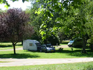 Wohnwagen und Auto auf einem Campingplatz im Grünen, umgeben von Bäumen und Rasenfläche.