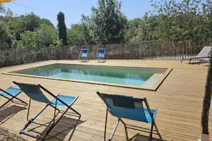 Schwimmbecken mit Holzdeck und zwei Liegestühlen am Pool, umgeben von Zaun und Bäumen im Campingbereich.
