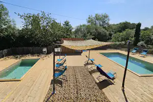 Zwei Holzterrassen mit zwei Swimmingpools, Liegestühlen und Sonnenschirm im Garten, umgeben von Hecken und Bäumen.