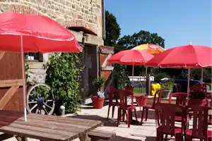 Rote Terrassenschirme vor einer Steinmauer, Holzbank und rote Stühle auf dem gepflasterten Platz.