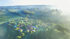 Luftaufnahme eines Campingplatzes in grüner Landschaft mit Bäumen, Wegen und mehreren Gebäuden im Hintergrund.