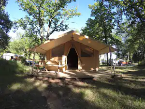 Campingzelt mit Vorzelt auf einem Stellplatz im Grünen, daneben eine Sitzbank und weitere Fahrzeuge zwischen Bäumen.