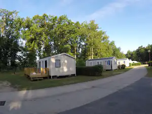 Mobilheime auf dem Campingplatz, Holzterrasse am Haus, Hecken und Bäume entlang des Weges.