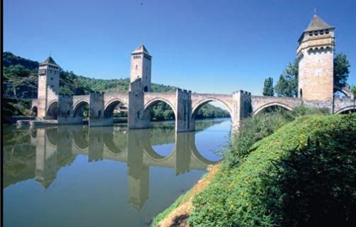 Mittelalterliche Steinbrücke mit mehreren Bögen über einem ruhigen Fluss, Spiegelung im Wasser und bewachsene Uferhänge.