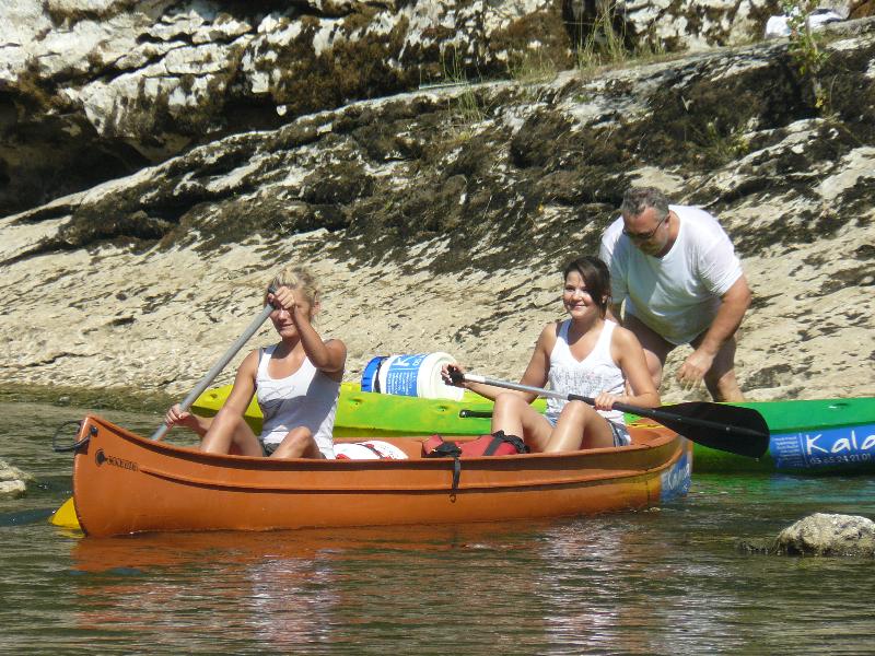 Kanu auf einem Fluss im Gebirge, drei Personen im Boot, Felsen am Ufer und steile Felswände im Hintergrund.