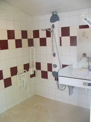 Camping-Badezimmer mit Dusche und Duschkopf, weißem Waschbecken und Handtuchhalter an gefliesten Wänden.