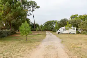 Wohnmobil auf einem Campingplatz-Stellplatz, Kiesweg und Rasenfläche zwischen Bäumen und Hecken.