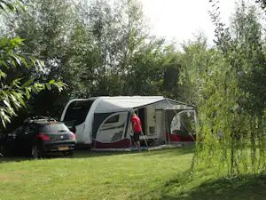 Campingzelt mit Vorzelt auf grünem Rasen, daneben ein Auto und weitere Zelte im Hintergrund zwischen Bäumen.