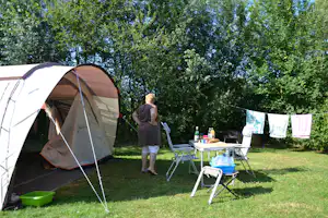 Campingzelt im grünen Garten, daneben Tisch mit Stühlen und Wäscheleine zwischen Bäumen.