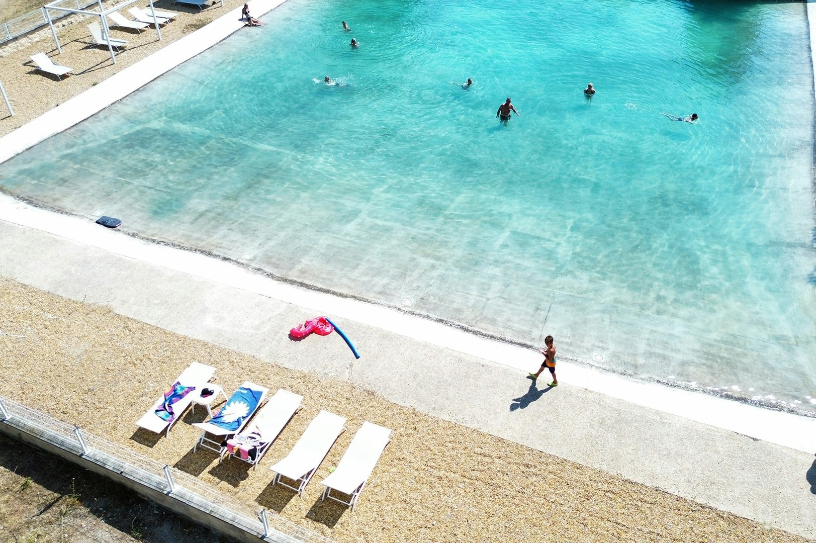 Schwimmbecken auf dem Campingplatz mit mehreren Liegen am Beckenrand und Personen im Wasser.