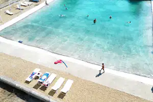 Schwimmbecken auf dem Campingplatz mit mehreren Liegen am Beckenrand und Personen im Wasser.