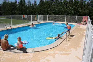 Kinder im Pool eines Campingplatzes, umgeben von Metallzaun und Liegen, mit Fliesen-Terrasse und Spielzeugschwimmringen.