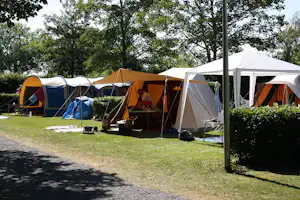 Mehrere Campingzelte auf einem Rasenplatz, daneben ein weißes Zelt und ein Tisch mit Campingausrüstung.
