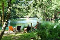 Camping La Coutelière - Camper liegen auf den Liegestühlen am Flussufer auf dem Campingplatz