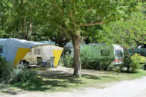 Gelbes Zelt auf einem Campingplatz, daneben Stühle und Tisch, im Hintergrund Wohnwagen und Bäume.