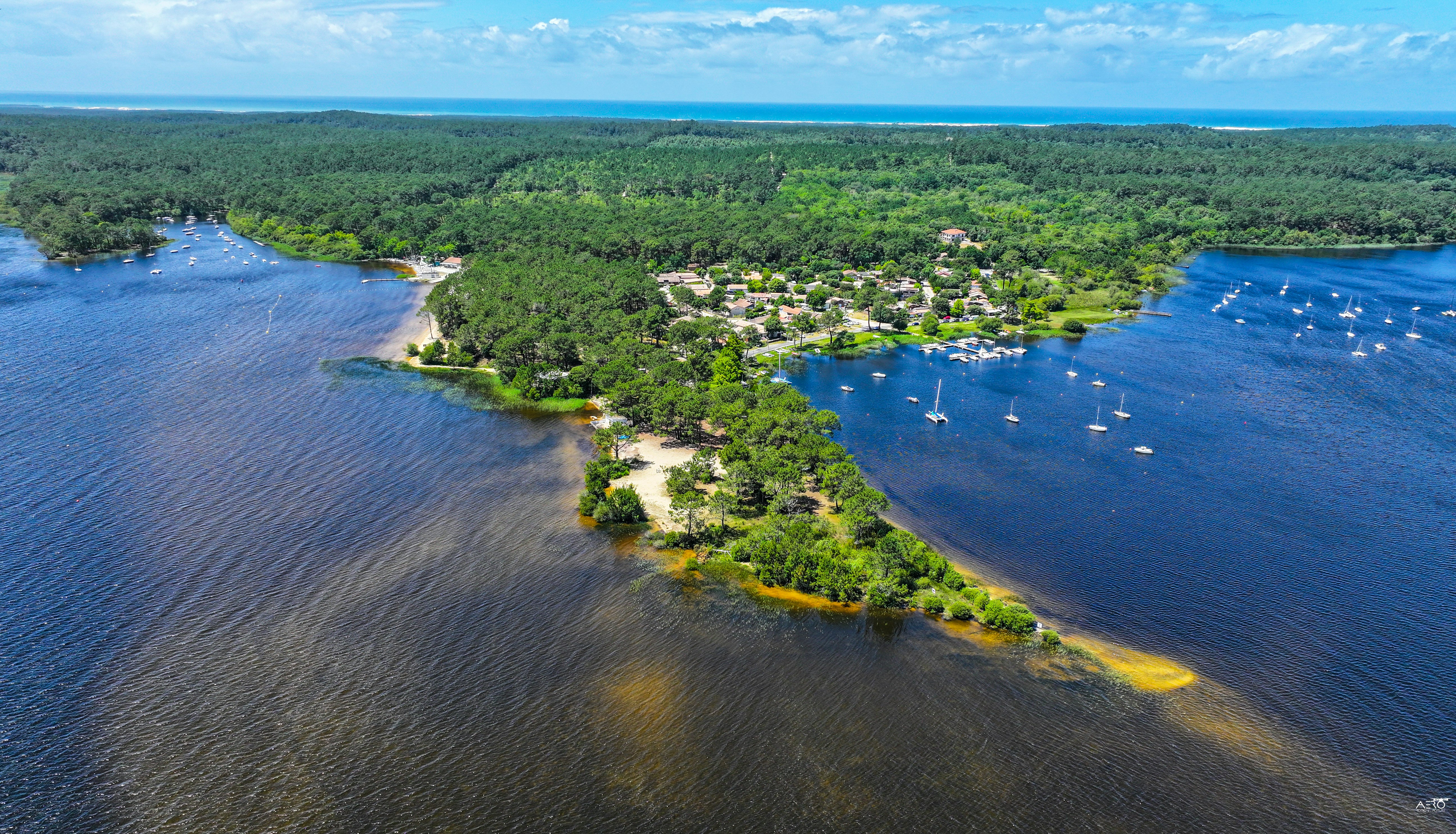 Luftaufnahme eines Campingplatzes am Seeufer mit Booten im Wasser und vielen Stellplätzen zwischen Bäumen.