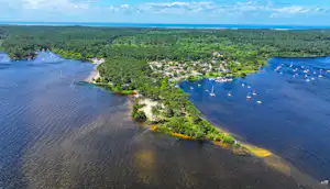 Luftaufnahme eines Campingplatzes am Seeufer mit Booten im Wasser und vielen Stellplätzen zwischen Bäumen.