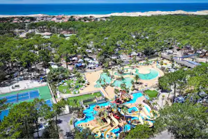 Großes Campinggelände mit mehreren Pools, Rutschen und Liegen, umgeben von Bäumen und kleinen Wegen, nahe am Meer.