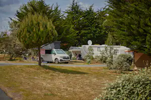 Wohnmobil auf einem Stellplatz im Grünen, daneben ein Wohnwagen und Hecken, Rasenfläche und Bäume im Hintergrund.