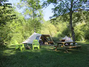 Zelte auf einem Campingplatz zwischen Bäumen, mit Picknicktisch und Stühlen auf dem grünen Rasen.