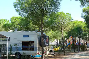 Wohnwagen auf einem Campingplatz zwischen Bäumen, mit Vorzelt, Stühlen und Tisch am Stellplatz.