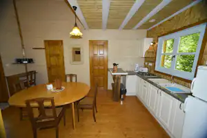 Holzhaus-Küche mit Küchenzeile, Fenster und Esstisch mit Stühlen im Innenraum.