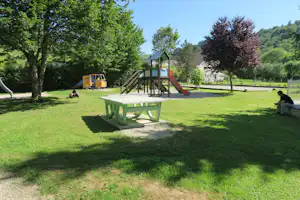 Spielplatz mit Rutsche und Klettergerüst, daneben ein grüner Picknicktisch auf dem Campingplatz im Schatten der Bäume.