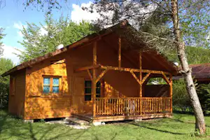 Holzferienhaus mit Veranda und Geländer, umgeben von Rasen und Bäumen, mit Fenstern und Holzfassade im Grünen.