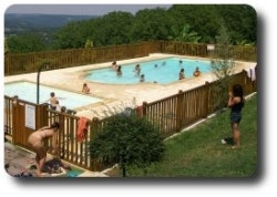 Schwimmbecken mit mehreren Liegen am Campingplatz, umgeben von Zaun und Bäumen, daneben ein Weg und Sitzbereich.