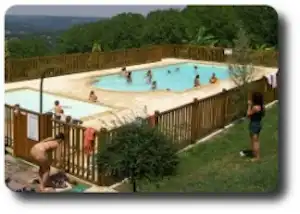 Schwimmbecken mit mehreren Liegen am Campingplatz, umgeben von Zaun und Bäumen, daneben ein Weg und Sitzbereich.