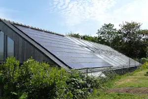 Große Solaranlage auf dem Dach eines Holzgebäudes im Campingbereich, umgeben von Büschen und Rasen.