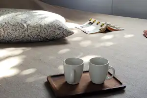 Bett im Campingzimmer mit zwei Kaffeetassen auf einem Tablett, daneben Kissen und Vorhang am Fenster.