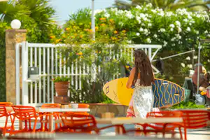 Camping La Gaviota - Camperin mit Surfbrett läuft an der Terrasse entlang