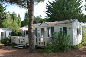 Ein weißes Mobilheim mit Terasse im Schatten unter dem Baum auf dem Camping La Grainetière