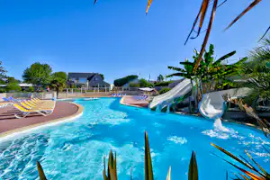 Blauer Camping-Pool mit Liegen am Rand, Palmen und Gartenpflanzen, im Hintergrund Gebäude und Zaun.
