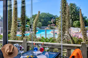 Terrasse mit gedecktem Tisch, Blick auf den Pool und hohe Zypressen im Garten.