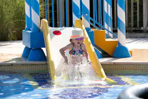 Yelloh! Village La Grange de Monteillac - Kind rutscht auf einer kleinen Wasserrutsche im Kinderbecken des Freibades