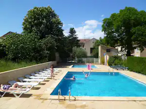 Schwimmbad mit blauem Wasser, Liegen auf der Terrasse und Blick auf Gebäude und Bäume im Campingbereich.