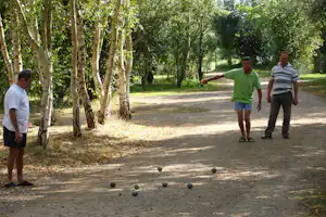 Boulespiel auf einem Kiesweg im Campinggelände, zwei Männer stehen zwischen Bäumen und Kugeln.