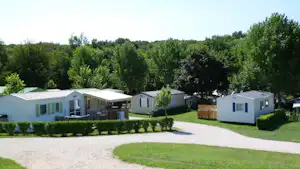 Reihe von Wohnwagen und Mobilheimen auf einem Campingplatz, mit Kieswegen, Rasen und grünen Bäumen im Hintergrund.