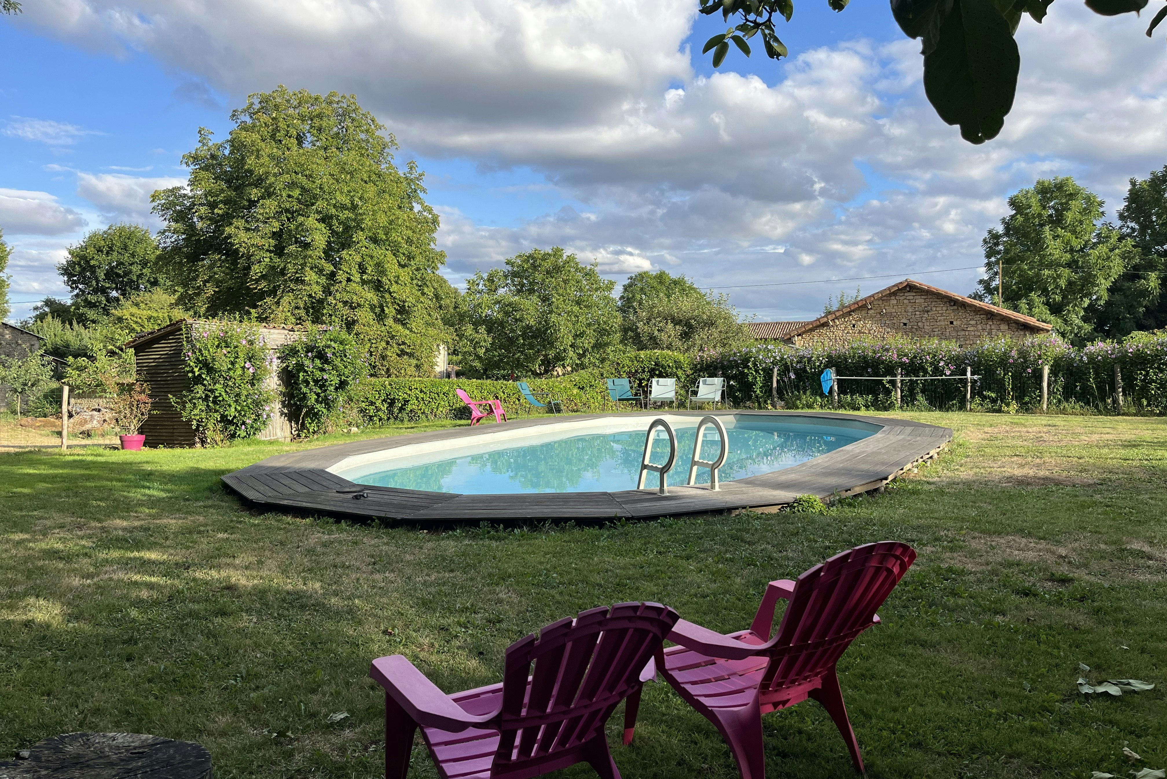 Camping-Pool im Garten mit Liegen, Rasenfläche und Bäumen, im Hintergrund ein Gebäude mit Holzfassade.