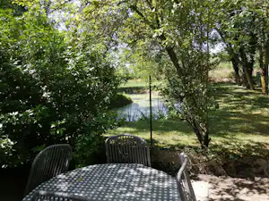 Terrasse mit Tisch und Stühlen am Campingplatz, Blick durch Bäume auf einen kleinen See.
