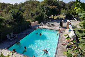 Schwimmbecken mit Liegen am Rand, Kinder im Wasser und Bäume im Hintergrund auf dem Campingplatz.