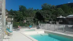 Camping-Pool mit türkisfarbenem Wasser, weißen Liegen und Sonnenschirmen, umgeben von Zaun und Bäumen im Hintergrund.